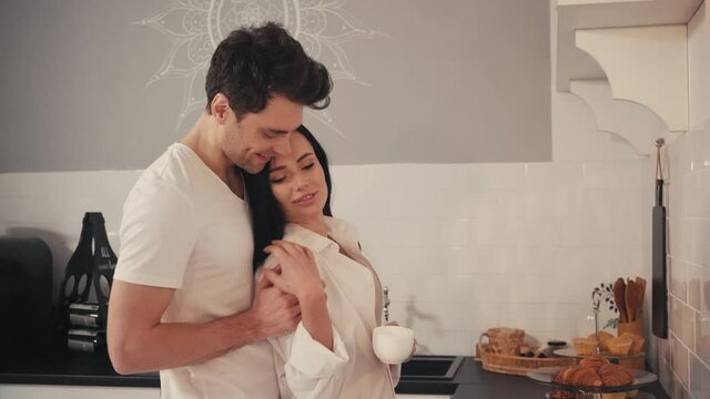 young man seducing sensual girlfriend drinking coffee in kitchen