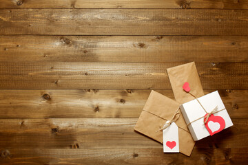 White gift box, gift and envelope wrapped in brown craft paper, tied with twine with bows and labels with red paper hearts on wooden boards. Love, Valentine's, women's day, relations, romantic