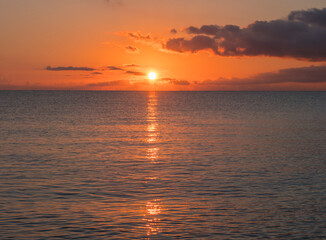 Sunrise with the red orange sun raising up from the sea with dark clouds at beach Spiaggia di Santa Maria Navarrese, Sardinia, Italy