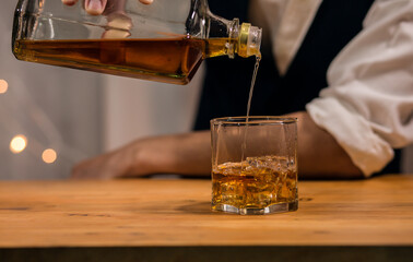 Barman pouring whiskey wearing protective mask on the bar counter