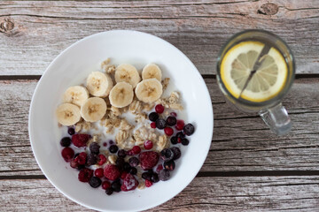 Oatmeal with banana pieces and berries, drenched in milk. Next to a glass of water with lemon
