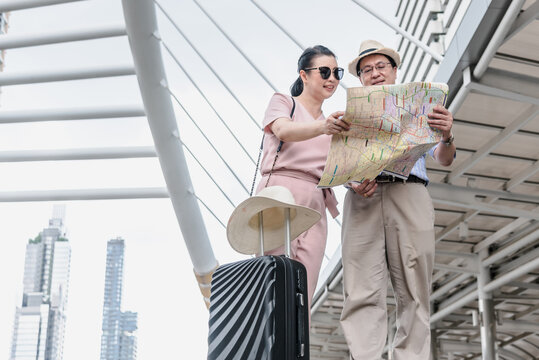 Asian Couple Retirement Age, Tourists Are Happy And  Looking At The Map For Plan A City Trip, To Travel And Elderly Concept.