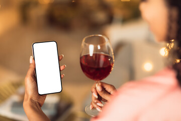 Black woman holding phone with empty white screen, drinking wine