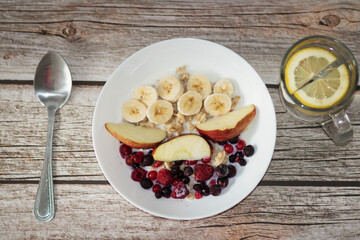 Oatmeal with banana pieces and berries, drenched in milk. Next to a glass of water with lemon