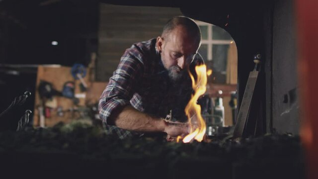 Male blacksmith lighting wood kindling to start blaze in forge - shot in slow motion