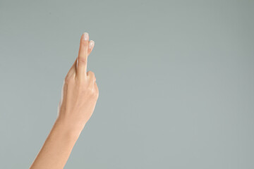 Woman with crossed fingers and space for text on grey background, closeup. Superstition concept
