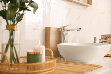 Fototapeta na wymiar Vase with beautiful branches, candles and fresh towels near vessel sink in bathroom. Interior design