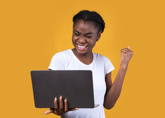 Joyful African Lady Holding Laptop Gesturing Yes Over Yellow Background