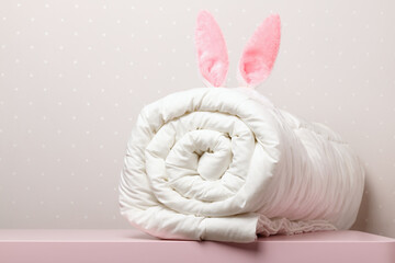 On the table lies a folded warm duvet with Easter bunny ears. Blanket for the bed. Copy space.