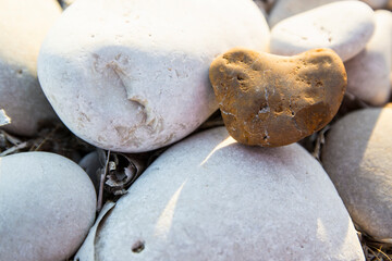 Valentines Day background with yellow stone heart among river or sea pebble stones