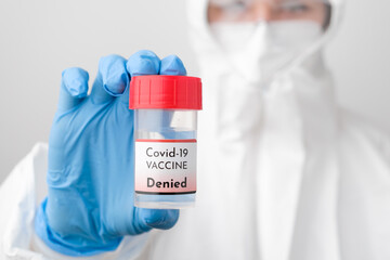 Denied Covid 19 vaccine bottle in doctors hand. Doctor in protective suit, face mask, safety...