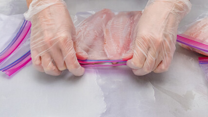 Fresh raw fish fillet in zip lock bags. Tilapia fillet on light marble background, close up. Woman hands put  fillet in zip lock bags for freezing © Hanna Tor