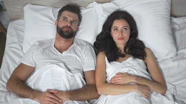 top view of confused man lying near embarrassed young woman in bed