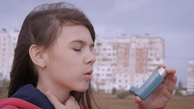 Suffering From Asthma In The City. A Teenage Girl With An Asthma Attack Uses An Inhaler.