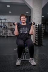 Fototapeta na wymiar an elderly woman in the gym is engaged in fitness with dumbbells in her hands