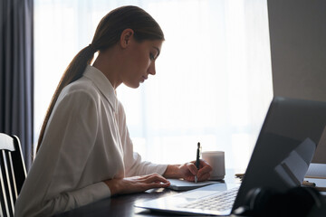 Side view of charming lady doing remote work on laptop