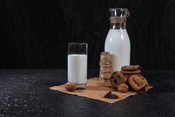 Fresh tasty milk in glass and bottle placed on table with cookies and chocolate on black background in studio  