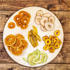 Tray with dried slices of orange, apple, pineapple, peach and banana on a wooden background. Fruit chips. Healthy and fashionable snack. Super food, top view