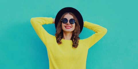 Portrait of beautiful young woman wearing a black round hat, yellow sweater on a blue background