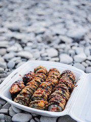 Popular Asian dish for eating with chopsticks. Hot baked rolls in plastic white takeaway container. Japanese raw fast food.