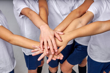 cropped team of young soccer players wish for good game, hold hands together, wearing uniform....