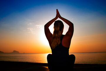 Woman sitting in lotus position meditating, with the amazing background of ocean and sunrise. Concept of healthy spiritual life and peace with nature