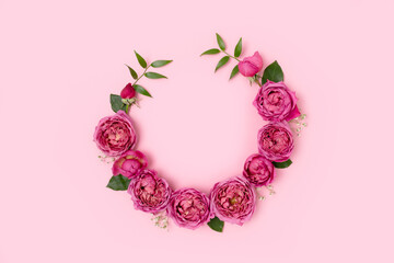 Round frame made of rose and green leaves on a pink pastel background. Flower wreath concept.