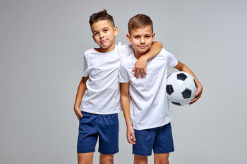 two friendly children soccer players posing at camera isolated on gray background. kids sport...