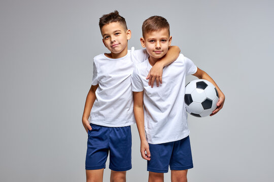 two friendly children soccer players posing at camera isolated on gray background. kids sport family leisure lifestyle concept. copy space advertisement