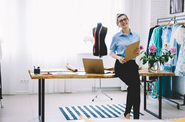 Cheerful dressmaker in creative workplace with clothes