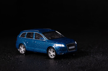 Fototapeta na wymiar Miniature model of a blue SUV car on a black background with water drops and rain. bad weather and sports car concept