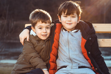 Two cute boys, brothers, sitting on a bench, being affectionate with each other.