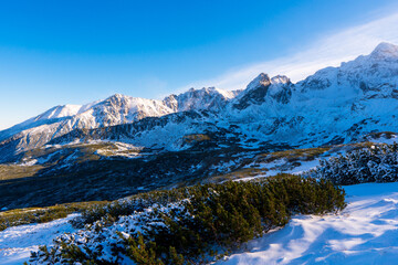 Winter mountain landscape. Sun shines through mountain peak at snowy hills. Winter scene in Tatra mountains, Poland.