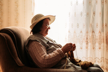 Elderly woman knitting sweater for her grandchildren by the window