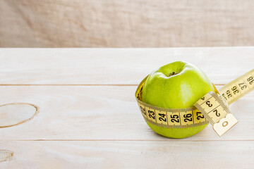 Green apple wrapped with a centimeter tape on a wooden desk.