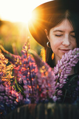 Portrait of woman with lupine bouquet in sunset light in countryside field. Atmospheric moment