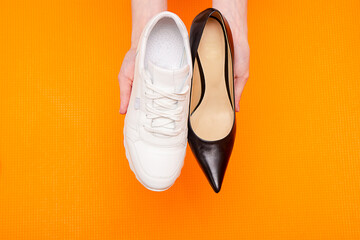 hands hold sneaker and shoe, concept of choice between comfort and business style for woman, orange...