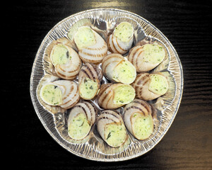many freshly prepared grape snails with green oil and garlic lie in a silver container on a black background top view . food in france snails in burgundy