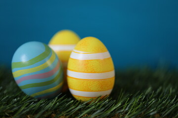 Easter holiday. Easter yellow and blue striped eggs in green grass on a bright blue turquoise background.Spring festive easter background.Easter symbol. copy space.Easter holiday card blank.