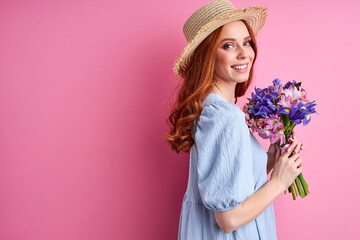 woman in blue dress enjoy flowers, posing isolated on pink background, smiling and looking at...