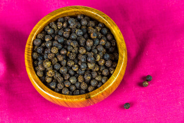 Small wooden bowl full of black peppercorns