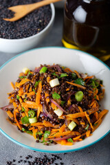 Black Lentil Salad with carrot, onion and parsley with bowl of black lentil on grey background.