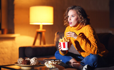 Young female eating French fries and watching interesting movie