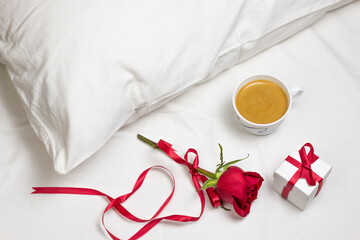 Cup of coffee, red rose with red ribbon and gift box on white bed. Romantic breakfast surprise for valentine day or holiday top view flat lay background