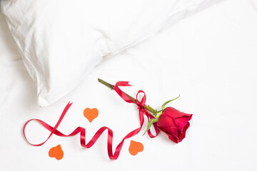 Red rose with red ribbon and little red heart on white bed. Valentine day or holiday romantic background.