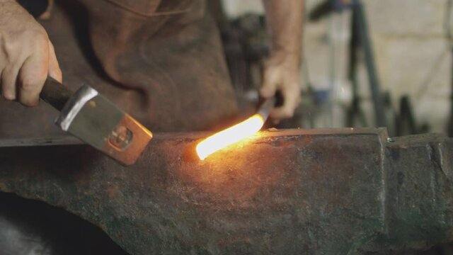 Close up of male blacksmith hammering red hot piece of metalwork on anvil - shot in slow motion