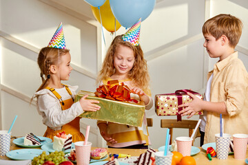 happy birthday party. children in party caps celebrating birthday at home in light room, kids with delicious food and gifts, congratulating