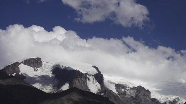 Tufted clouds float over snow-covered slopes of largest mountain in Europe. Elbrus on Sunny summer day. Shooting at 4 m A.S.L. Boundary of melting of glaciers (mountain ice sheet ) is lower
