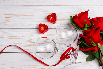 Valentine day romantic flat lay image. Wine glasses, heart shaped candles and red roses with red ribbon on white wooden background.
