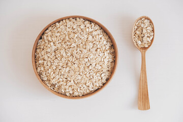 Dry oatmeal in a wooden plate and spoon on a white background. Top view. Copy, empty space for text